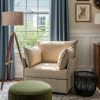 Beige Huddle armchair with cushions in a living room setting with a tripod lamp and decorative items.